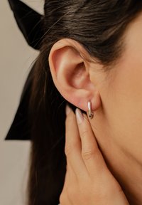 Srebrna kolczyk w kształcie obręczy o gładkiej, wypolerowanej teksturze. Zbliżenie uwydatniające okrągły kształt i minimalistyczny design.