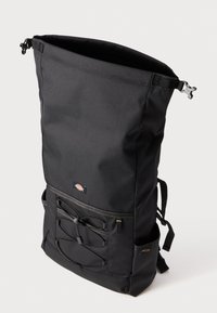 Mochila preta com fecho superior, feita de tecido durável, com detalhes em corda elástica exterior, alças ajustáveis e um emblema na parte da frente.