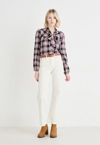 Camicia a quadri nei colori navy, rosso e bianco con un dettaglio a farfalla, abbinata a pantaloni a gamba larga crema e stivaletti ankle brown. Texture morbide in tutto l'outfit.