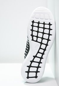 Svart och vit atletisk skosula med en texturerad vit gummibas och ett rutmönster i svart för grepp. Slät yta.