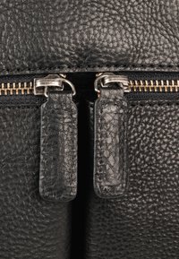 Bolso de cuero negro texturizado con cierre de doble cremallera y tiradores metálicos, y una pista de cremallera en tono dorado.