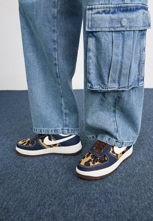 Adidași bleumarin cu accente de leopard, sigla albă Nike, șireturi maro și talpă intermediară albă. Asortați cu pantaloni cargo din denim deschis.