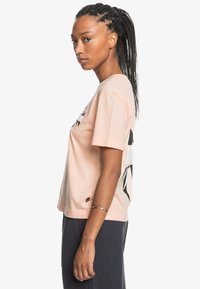 Short-sleeve, pastel pink cotton t-shirt featuring black graphic design on front. Boxy cut with a round neck and straight hemline.