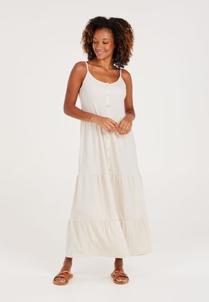 Light beige maxi dress with spaghetti straps, button front, textured fabric, and a tiered bottom. Worn with brown strappy sandals.