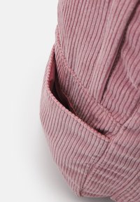 Gros plan d'une poche de vêtement en velours côtelé rose poussiéreux, avec des rainures verticales et des coutures visibles le long des bords.