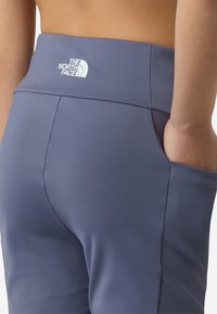 Høytlivs leggings i skiferblått stretchstoff, med synlig logo på linningen og en sidelomme for bekvemmelighet.