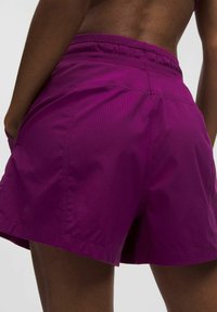 Pantalones cortos morados hechos de una tela ligera y texturizada. Presenta una cinturilla elástica y bolsillos laterales. Detalle sutil del logo en el dobladillo.