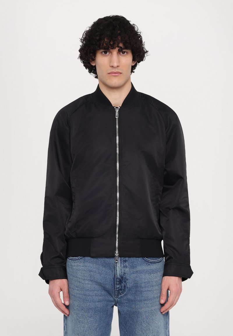 Zwarte bomberjack met een rits aan de voorkant, ribgebreide boorden en tailleband. Gemaakt van glad nylonmateriaal en heeft een eenvoudig ontwerp.