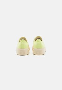 Grüne Leinensneaker mit niedrigem Schnitt und beige Gummisohle, die eine strukturierte Oberfläche aufweisen und mit dem eingeprägten "Converse All Star"-Logo an der Ferse versehen sind.