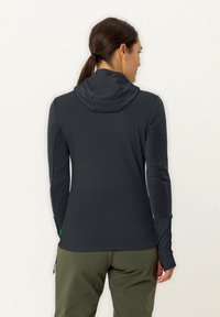 Dunkelgrauer, taillierter Hoodie aus strukturiertem Stoff, mit hohem Kragen und langen Ärmeln, ausgestattet mit Daumenlöchern und einem kleinen grünen Logo in der Nähe des Saums.