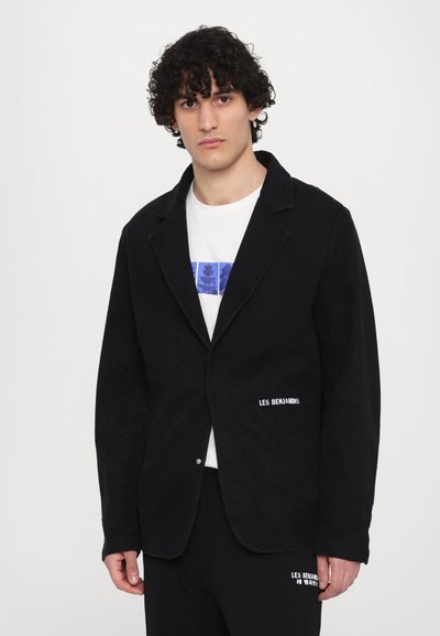 Veste noire avec revers en notch, tissu texturé, fermeture à un bouton, et logo "LES BENJAMINS" brodé sur le devant.