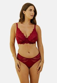 Soutien-gorge en dentelle rouge et culottes assorties avec un motif floral et des bords festonnés. Bretelles réglables et quincaillerie décorative au centre.