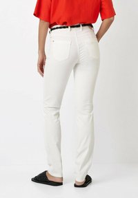 Weiße Denim-Jeans im geraden Schnitt, mit Gesäßtaschen und Reißverschluss. Kombiniert mit einem roten Oberteil und schwarzen Rutsch-Sandalen.