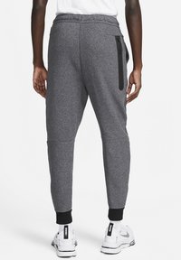 Šedé sportovní tepláky s texturovaným povrchem, zúženými nohavicemi, elastickým pasem a zapínacím bočním kapsou na zip. Dokončené černými manžetami.