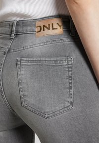 Grå denimjeans med medelhög midja, en liten bakficka och en fusk läderetikett med prägling på midjebandet.