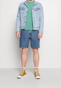 Vaaleansininen farkkutakki, vihreä T-paita, siniset farkkushortsit ja ruskeat korkeat tennarit. Rentoa, kerroksellista asua, jossa on selkeitä värejä ja tekstuureja.