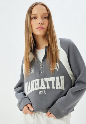 Grå zip-up sweatshirt med hvide accenter og "MANHATTAN USA" trykt på fronten. Blandingsbomuld, afslappet pasform, ribbede manchetter.