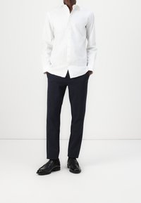 Vit långärmad skjorta med knappar, marinblå randiga byxor och svarta loafers. Glatt tyg, skräddarsydd passform och kontrasterande färger.