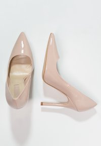 Nude patentläder högklackade skor med spetsig tå och smal stilettklack. Slät textur med en glansig yta.