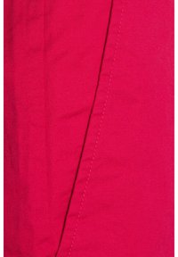 Tejido texturizado en rosa con un patrón tejido y detalles de costura visibles. La superficie parece suave con un ligero brillo.