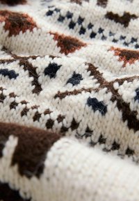 Knitted sweater fabric featuring a cream base with dark brown and navy geometric patterns, showcasing a textured, warm design.
