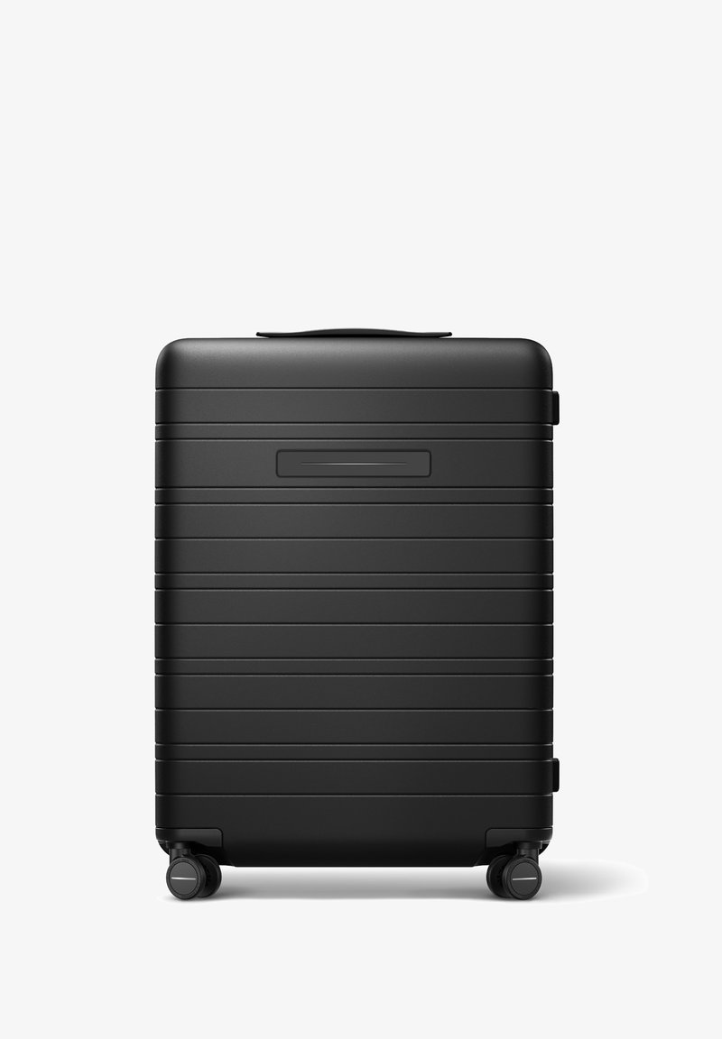 Valise rigide noire avec des rainures horizontales, une poignée robuste sur le dessus et quatre roues rotatives à 360 degrés pour une maniabilité facile.