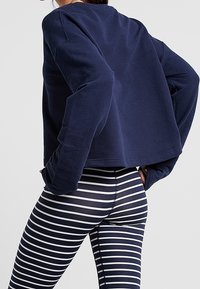 Sudadera corta de un color azul marino hecha de forro polar, combinada con unas mallas ajustadas a rayas en azul marino y blanco, que exhiben una textura suave y un diseño ajustado.