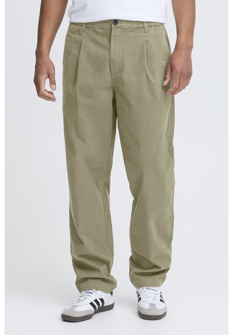 Pantalon large couleur vert olive clair, à texture lisse, avec des plis sur le devant, des passants pour ceinture et une fermeture par un seul bouton.