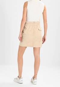 Falda texturizada beige con cinturilla elástica, que presenta un patrón de cuadros y un bolsillo lateral. Combinada con zapatillas blancas.