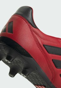 Scarpa da calcio sintetica rossa con colletto e dettagli neri. Parte superiore testurizzata e suola con motivo esagonale e tacchetti visibili per la trazione.