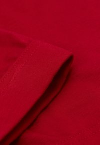 Tela de algodón roja con textura suave, que presenta un borde doblado y costuras visibles. El color es uniforme, sin patrones ni hardware distintivo.
