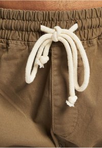 Pruunid elastse vöökohaga püksid, kus ees on paks valge punutud nöör lipsuks seotud.