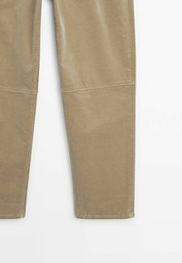 Partie inférieure d'un pantalon en velours côtelé marron clair avec des coutures visibles au niveau des genoux et une coupe droite, sur fond blanc.