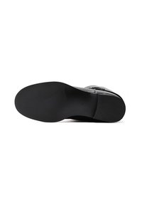 Suela de zapato negra con una superficie lisa y plana y patrones de agarre texturizados. Forma redondeada con un ligero tacón; detalle de tamaño en relieve visible.