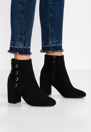 Musta mokkanahka nilkkaboots, joissa on terävä kärki, sivuvetoketju ja nauhoitussuunnittelu, jossa on metalliset silmukat. Läpiviennin muotoilu vakauden takaamiseksi.