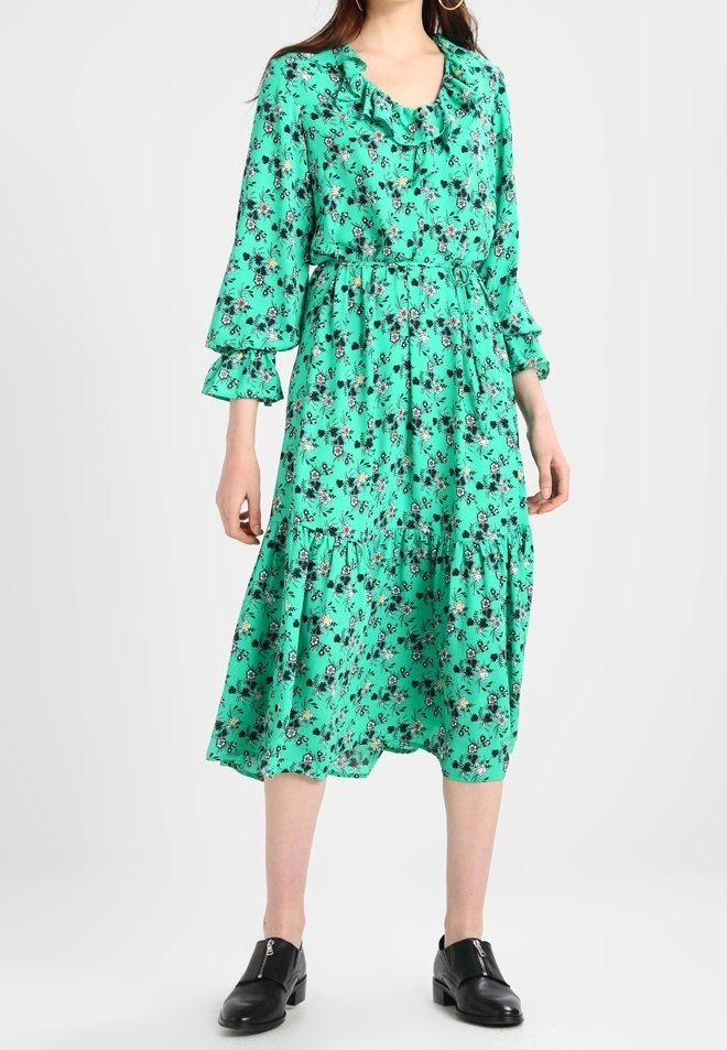 Robe midi florale vert menthe avec encolure à volants et manches longues évasées. Caractérisée par une taille cintrée et une jupe à volants. Agrémentée de fleurs noires.