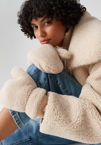 Beige Fleecejacke mit weitem Kragen und gestrickten Bündchen, kombiniert mit blauen Denim-Jeans. Der Stoff hat ein strukturiertes, flauschiges Aussehen.