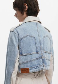 Chaqueta de mezclilla con un diseño recortado, color azul claro, dos bolsillos traseros y una etiqueta de cuero marrón en la cinturilla de Desigual.