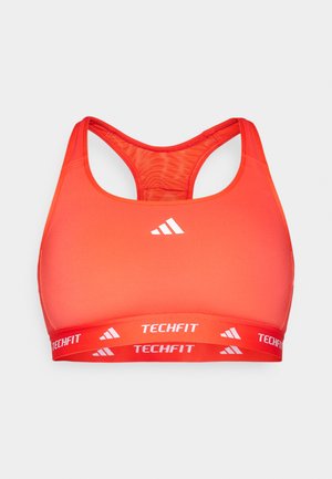 Reggiseno sportivo rosso con design racerback, realizzato in tessuto liscio. Presenta un logo bianco a contrasto e un elastico con marca etichettato "TECHFIT".