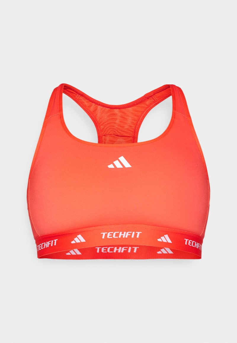 Soutien-gorge de sport rouge avec un dos nageur, fabriqué en tissu lisse. Il présente un logo blanc contrastant et une bande élastique de marque étiquetée "TECHFIT."