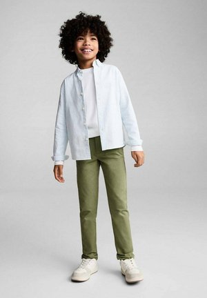 Camicia azzurra a righe con bottoni sopra una t-shirt bianca, abbinata a pantaloni verde oliva e sneakers bianche. Tessuto morbido, vestibilità casual.