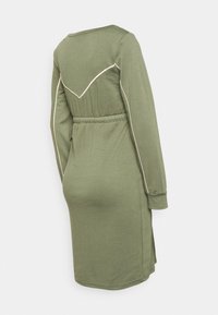 Vestido longo de mangas compridas em verde oliva com cintura ajustada, apresentando bainhas brancas contrastantes ao longo do yoke traseiro e fendas laterais. Textura de tecido suave.