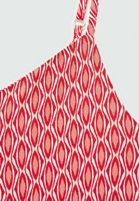 Punainen kuvioinen kangas, jossa on timanttimotiivi vaihtelevissa sävyissä ohuilla valkoisilla ääriviivoilla. Säädettävät hihnat ja sileä pinta.