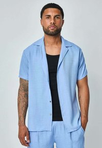 Chemise à manches courtes bleu clair à boutons avec une coupe décontractée ; associée à un débardeur noir. Texture lisse, design minimaliste et éclat subtil.