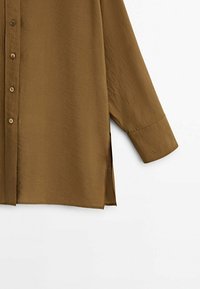 Chemise marron à boutons, fabriquée en tissu lisse et léger avec une finition légèrement brillante. Elle dispose de manches longues et d'échancrures sur les côtés à l'ourlet.