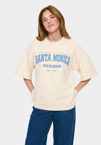 Krémové oversized tričko s modrým grafickým textem "SANTA MONICA STATE BEACH EST. 1909." Krátké rukávy a volný střih. Bavlněná tkanina.