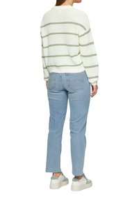Hellgrün gestreifter Strickpullover kombiniert mit mittelhohen hellblauen Jeans und weißen Sneakers mit grünen Akzenten. Lässiger Schnitt, sichtbare Saumdetails.