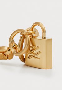 Gold padlock with a smooth, metallic finish, rounded shackle, and decorative initials engraved on the front. Attached to a thick gold chain.