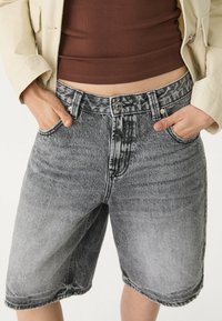 Shorts en denim gris clair avec une finition déchirée. Présente une taille haute, cinq poches et des coutures contrastantes. Fermeture à bouton standard.