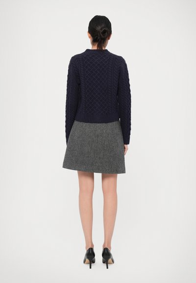 Navy cable-knit sweater with a round neck, cropped design, paired with a gray A-line skirt and black high-heeled shoes.